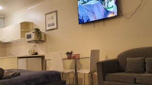 Una sala de estar con sofá, televisor montado en la pared, una mesita y una zona de kitchenette.