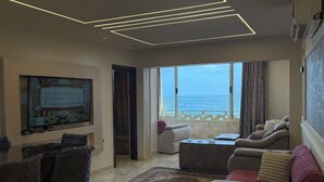 Un salon avec un canapé, une table basse, un tapis, un téléviseur et une vue sur la mer.