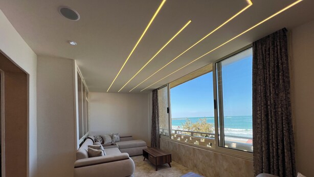 Un salon moderne doté d’une grande fenêtre, d’un ensemble de canapés, d’une table basse et offrant une vue sur la mer.