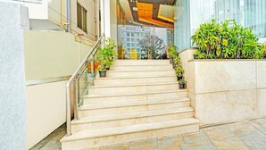 A set of marble stairs leading to a modern building entrance with glass walls and potted plants. - Classic With Twin Bedindiranagar (Bengaluru)