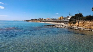Vista costera con aguas cristalinas, una playa de arena y edificios a lo largo de la orilla.