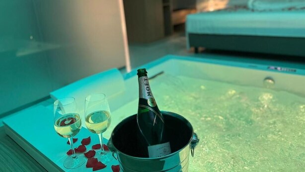 Una habitación con una cama, una mesita de noche con una botella de champán y copas, y una bañera.