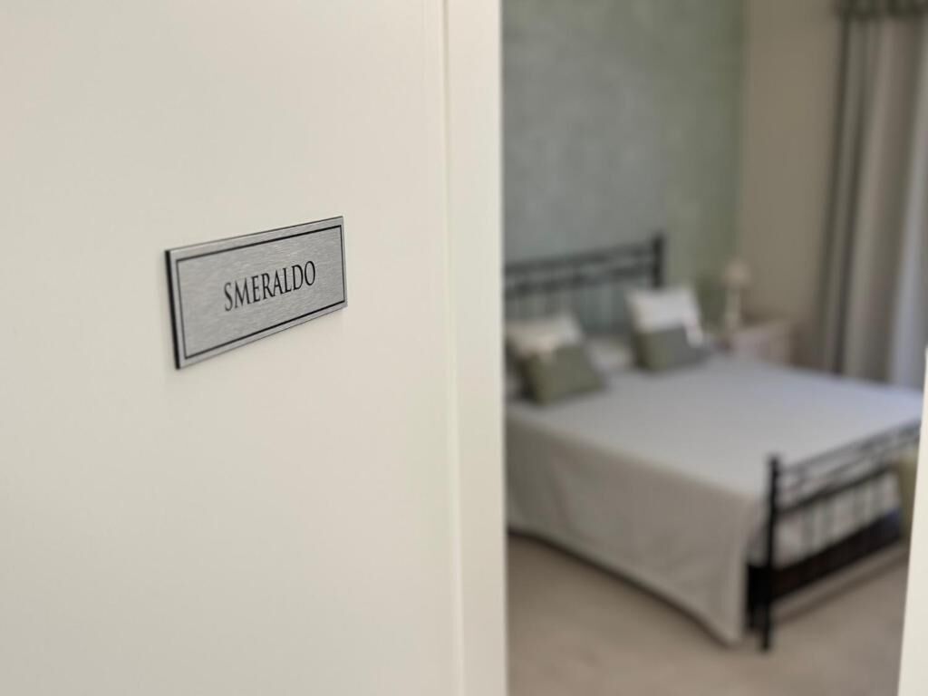 A room with a bed, a nightstand, and a wall-mounted sign that reads 'SMERALDO'.