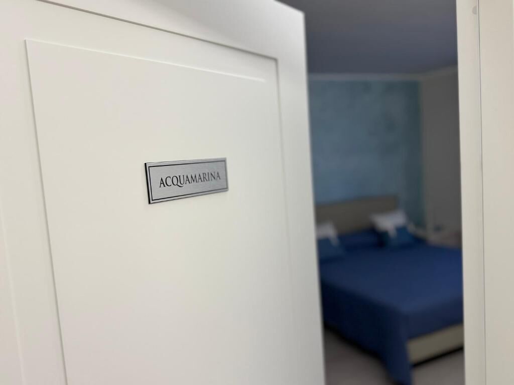 Una habitación con una cama, un edredón azul y un cartel en la puerta que dice 'ACQUAMARINA'.