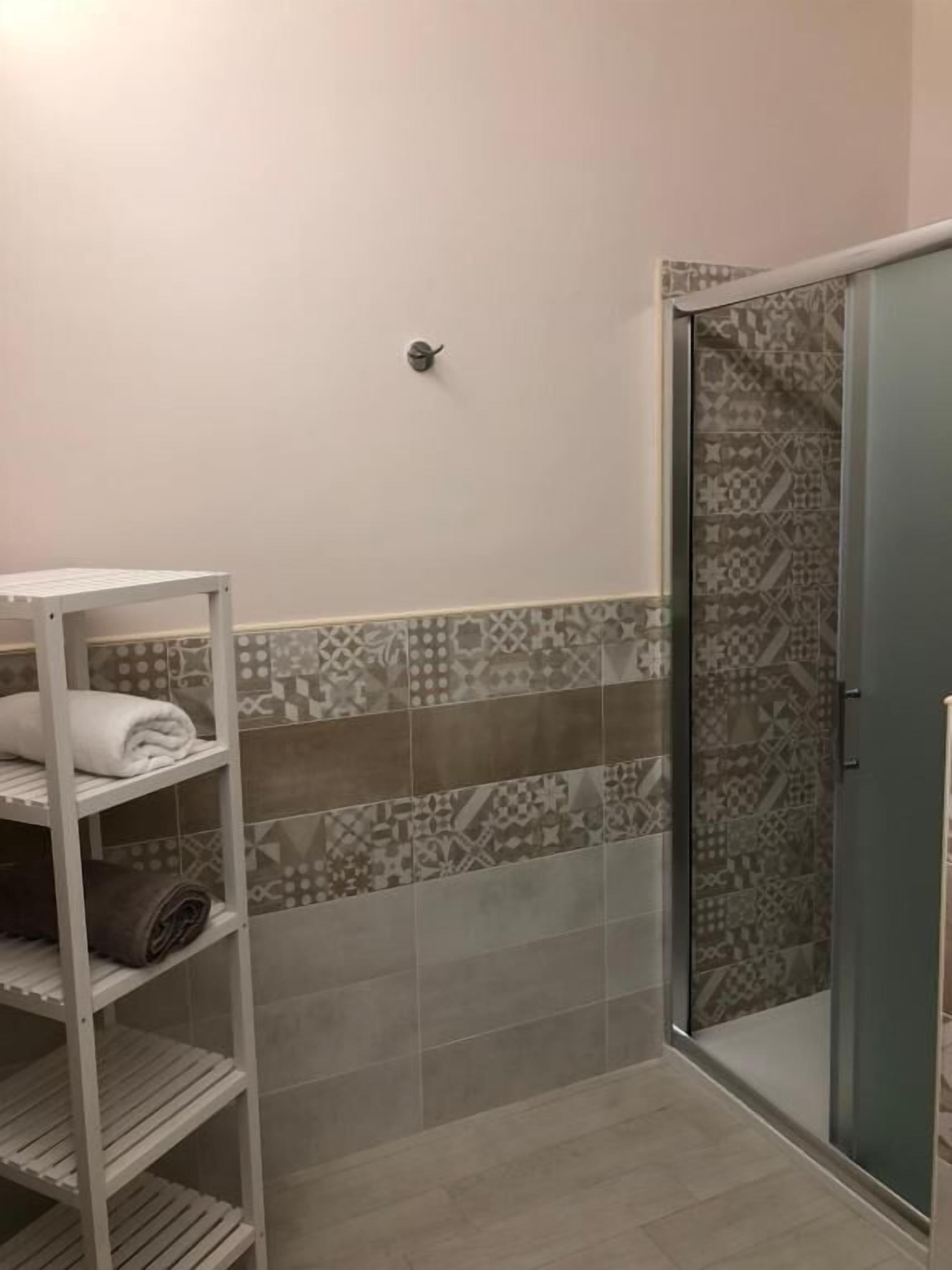 A bathroom with a shower, a towel rack, and a shelf with folded towels.