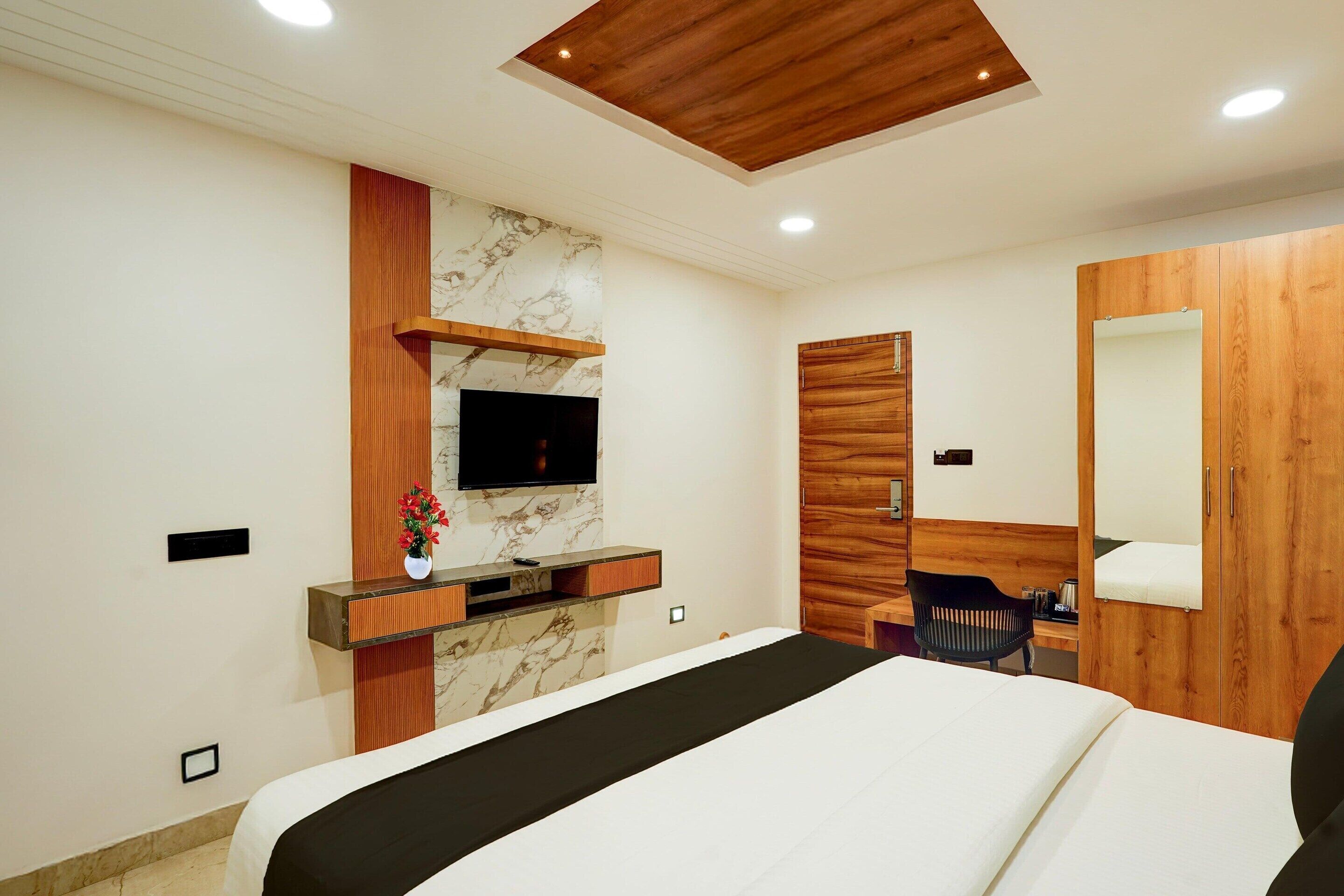 Una habitación de hotel moderna con una cama, un televisor montado en una pared de mármol, un armario de madera y un escritorio con una silla.