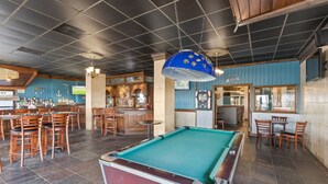 Une table de billard dans un espace bar, avec des chaises en bois et un comptoir.
