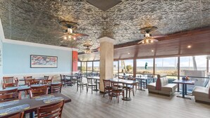 Un restaurant spacieux avec de hauts plafonds, des motifs décoratifs élaborés et de grandes fenêtres offrant une vue sur la plage.