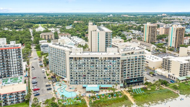 Un hôtel de grande hauteur, avec de nombreux étages, une piscine et un espace paysager agrémenté de palmiers.