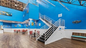 Un vaste espace intérieur abritant une piscine, avec un mur bleu, un escalier et un coin salon doté de chaises rouges.