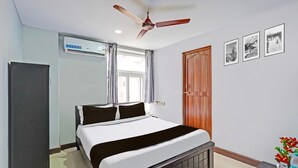 A bedroom with a bed, ceiling fan, window, air conditioning unit, wooden door, and framed pictures on the wall. - Deluxe spl Palace (Chennai)