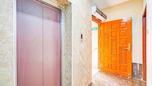 An elevator, a fire exit door, and a hallway with marble flooring. - Deluxe spl Palace (Chennai)