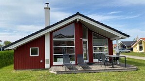 Un bâtiment rouge avec une grande fenêtre en verre, une cheminée et une terrasse avec des chaises.