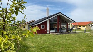 Une maison moderne avec une façade rouge, de grandes fenêtres et un patio couvert doté d’un espace salon extérieur.
