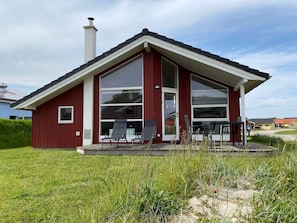 A modern house with a red exterior, large windows, and a covered patio area. - Scandinavian Home Near the Coast (Grossenbrode)
