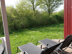 Ein überdachter Außenbereich mit zwei schwarzen Liegestühlen und einer Holzterrasse.