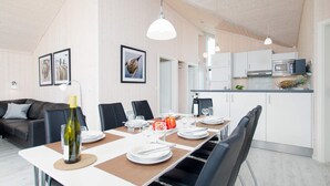 A dining area with a table set for four, kitchen cabinets, a microwave, and a refrigerator in the background. - 4 Star Holiday Home in Grossenbrode (Grossenbrode)