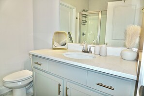 Une salle de bain comprenant des toilettes, un lavabo, un meuble-lavabo, un miroir et une douche.