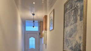 A hallway with a door, a light fixture, a framed picture, and a tiled floor.