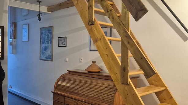 A wooden staircase with a desk and shelving unit in a room with tiled flooring and wall-mounted artwork.