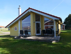 A yellow building with a red roof, large windows, and a deck with chairs. - 4 Star Holiday Home in Grossenbrode (Grossenbrode)