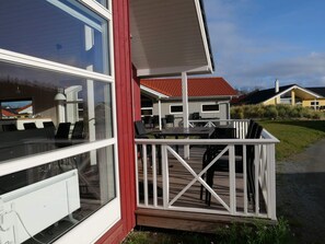 En modern byggnad med stora fönster, en träveranda och utomhusmöbler.
