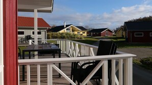 A wooden deck with outdoor furniture, a white railing, and a view of houses in the background. - 4 Star Holiday Home in Grossenbrode (Grossenbrode)