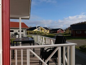 A wooden deck with outdoor furniture, a white railing, and a view of houses in the background. - 4 Star Holiday Home in Grossenbrode (Grossenbrode)