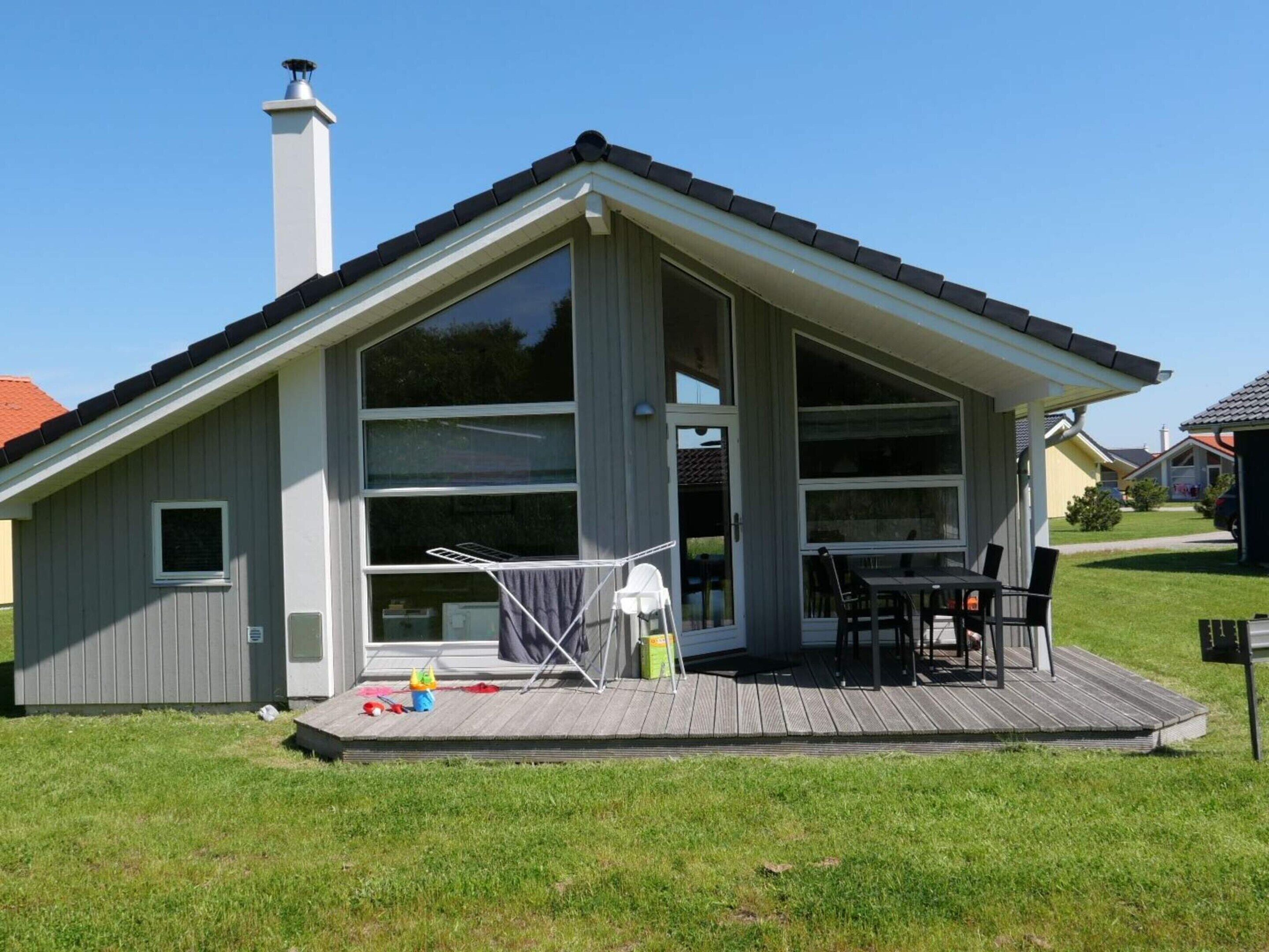 Ett envåningshus med en stor veranda på framsidan, en skorsten och en skjutdörr av glas.