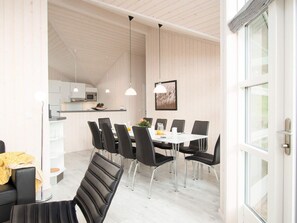 A modern dining area with a white table, black chairs, pendant lights, and a kitchen in the background. - 4 Star Holiday Home in Grossenbrode (Grossenbrode)
