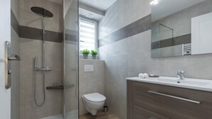 Un baño moderno con cabina de ducha de vidrio, inodoro, lavamanos con espejo y armarios de madera.
