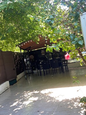 A covered outdoor seating area with chairs and a table, surrounded by greenery and a fence. - La Terrasse, your cosy nest 10 minutes from train stations, old town and beaches (Antibes)