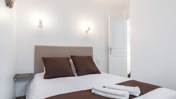 Una cama bien hecha con cabecera marrón, ropa de cama blanca y una toalla doblada sobre la cama.