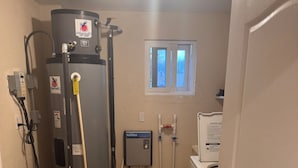 Un baño con un calentador de agua grande, un inodoro, un lavamanos y una ventana.