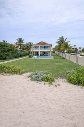 Une maison à deux étages avec une piscine, entourée d’une pelouse bien entretenue et de palmiers.