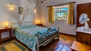 A bedroom with a bed, bedside lamps, a window with curtains, a fan, and a wooden ceiling. - Algarve Apartment With Garden & Pool (Portimão)