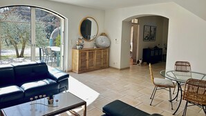 Ein modernes Wohnzimmer mit einer Couch, einem Couchtisch, einem Esstisch und Stühlen. Es gibt ein großes Fenster, einen Spiegel und eine Kommode.