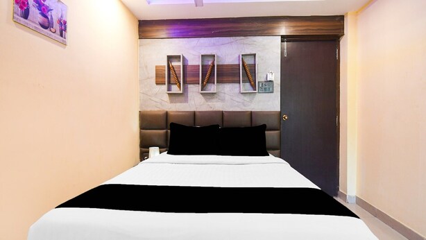 A modern hotel room with a bed, a ceiling fan, a marble wall, and a door. - Super Deluxe Room Super Collection O (Gobindpur)