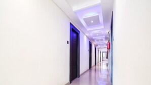 A long, narrow hotel corridor with doors on one side and a fire extinguisher on the other. - Super Deluxe Room Super Collection O (Gobindpur)