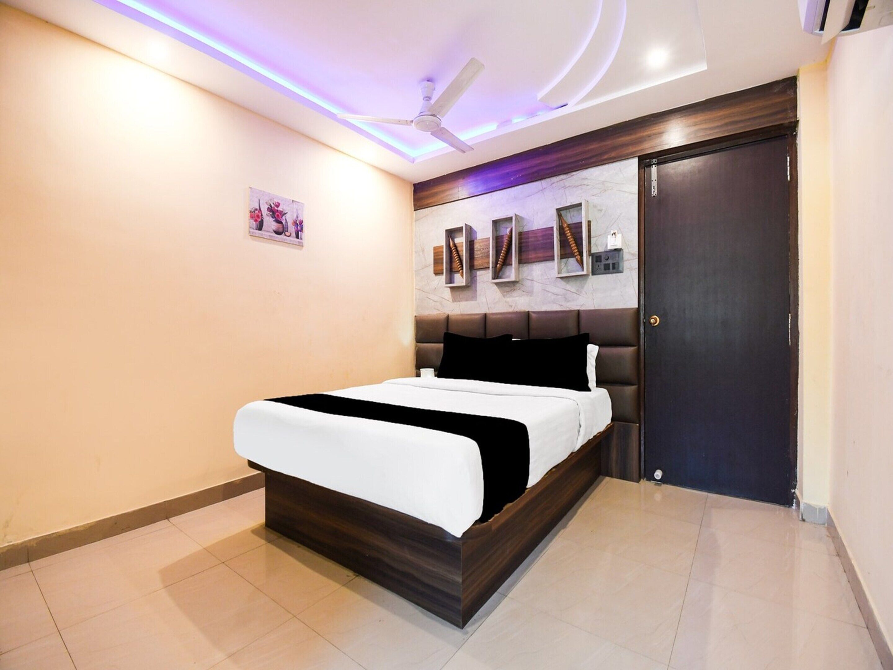 A bedroom with a bed, a ceiling fan, a dark door, and a wall-mounted shelf with decorative items.