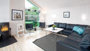 A modern living room with a fireplace, a sofa, a dining table, and a large window. - Villa With Private Sauna for Ten (Grossenbrode)