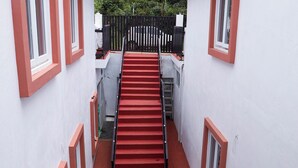 Uma escada estreita com degraus vermelhos que leva a um prédio branco com janelas emolduradas em vermelho.