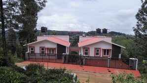 Um edifício de dois andares com telhado vermelho e paredes brancas, rodeado por vegetação.