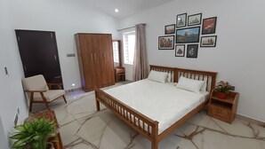 Quarto com cama de madeira, uma cadeira, guarda-roupa, mesa pequena e planta em vaso.
