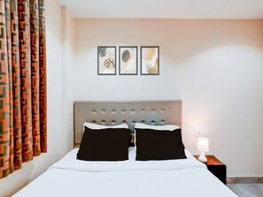Une chambre d’hôtel avec un lit, une table de chevet, une lampe et trois œuvres d’art encadrées accrochées au mur.