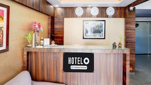 A hotel reception desk with clocks, a framed picture, and a sign indicating it's company-serviced. - Single Room Olivia Comforts (Bengaluru)