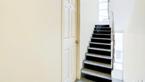 A narrow hallway with a white door and a black staircase leading to an upper floor. - Single Room Olivia Comforts (Bengaluru)