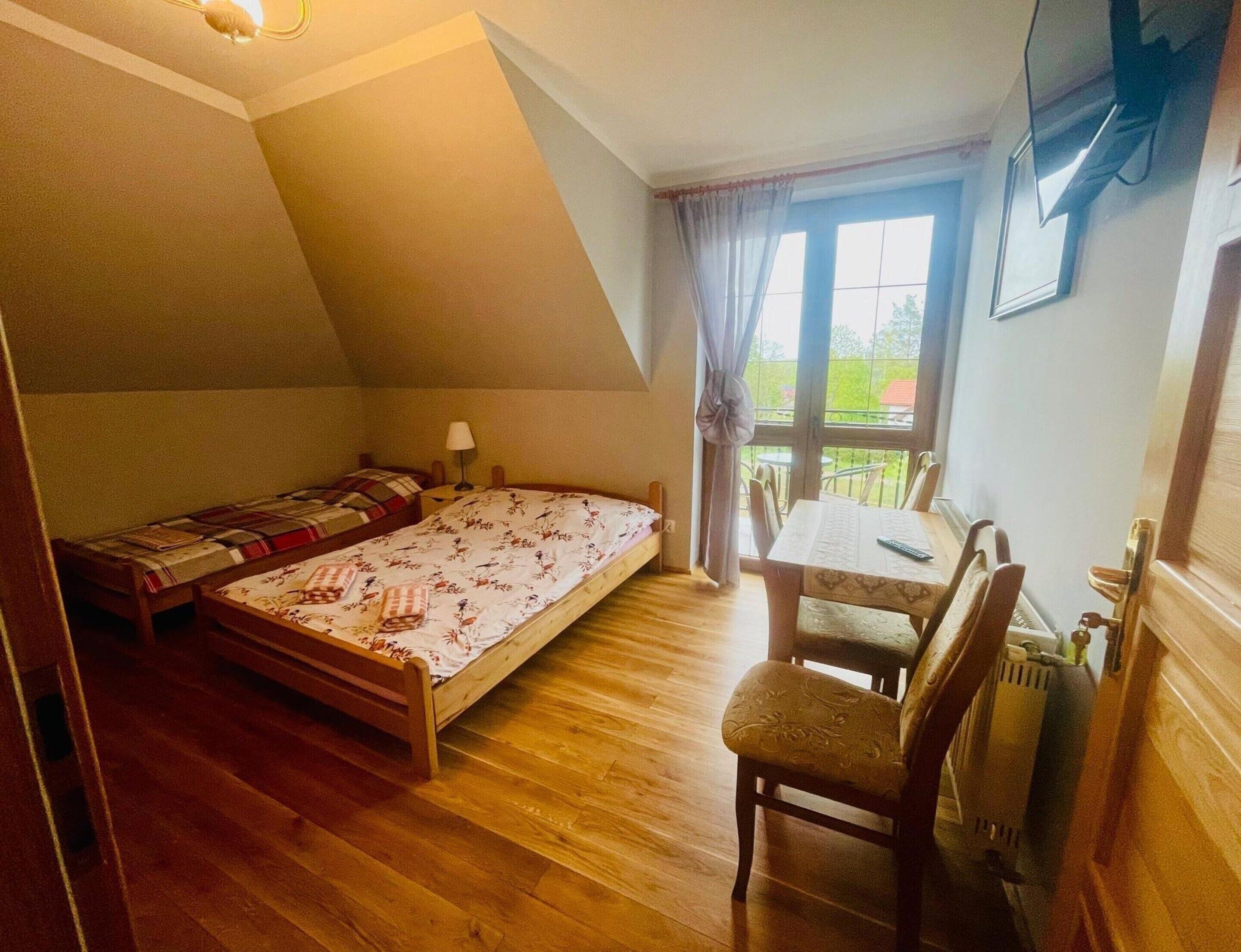 A room with a bed, a table with chairs, a window with curtains, and a radiator.