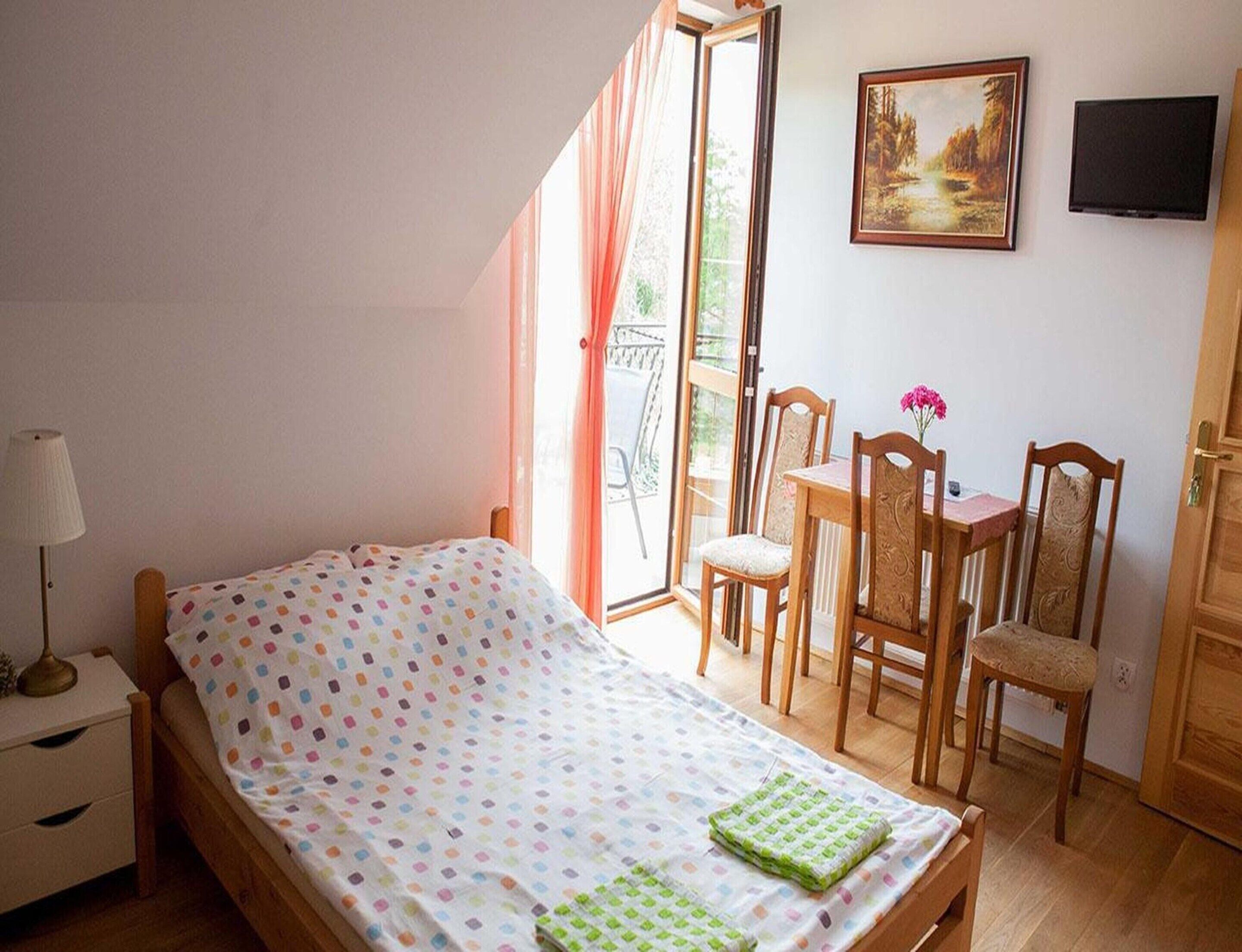 Une chambre à coucher avec un lit, une table de chevet, une chaise, une petite table avec un vase, un tableau au mur et un téléviseur.