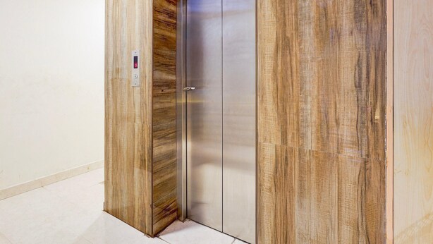 Een moderne lift met een metalen afwerking en houten lambrisering aan de zijkanten.